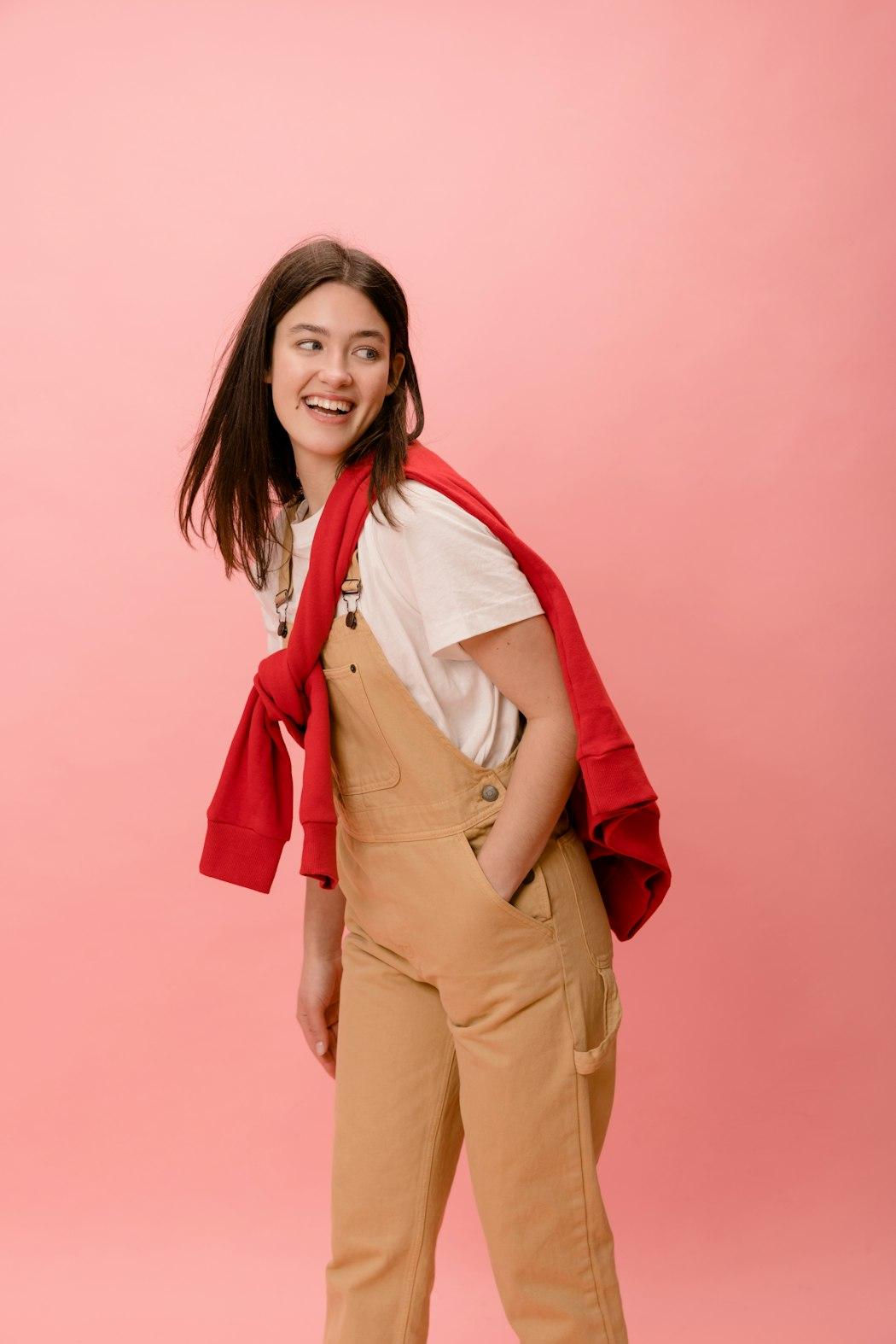 Woman in an everyday layered outfit against a pink background